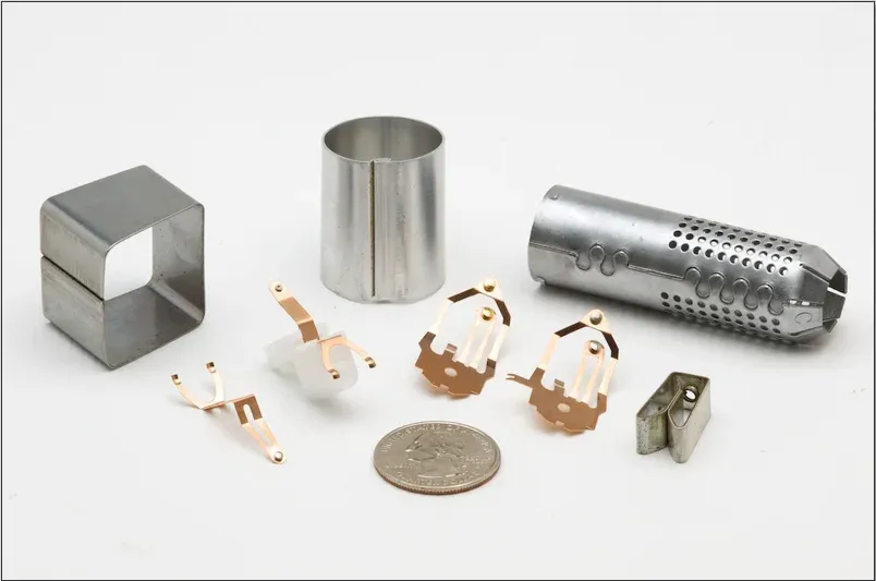 Assorted precision metal stampings, formed shells, and clips shown with a coin for scale