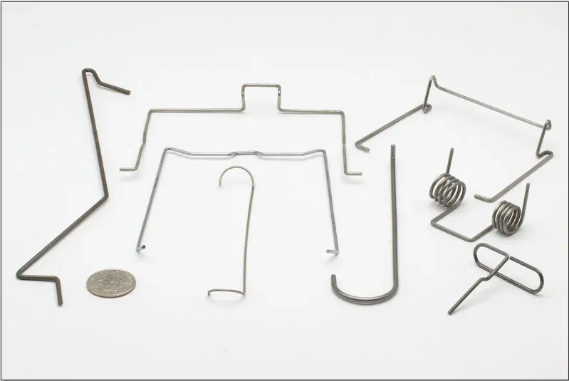 Custom bent wire forms, hooks, and torsion wire clips shown with a coin for scale